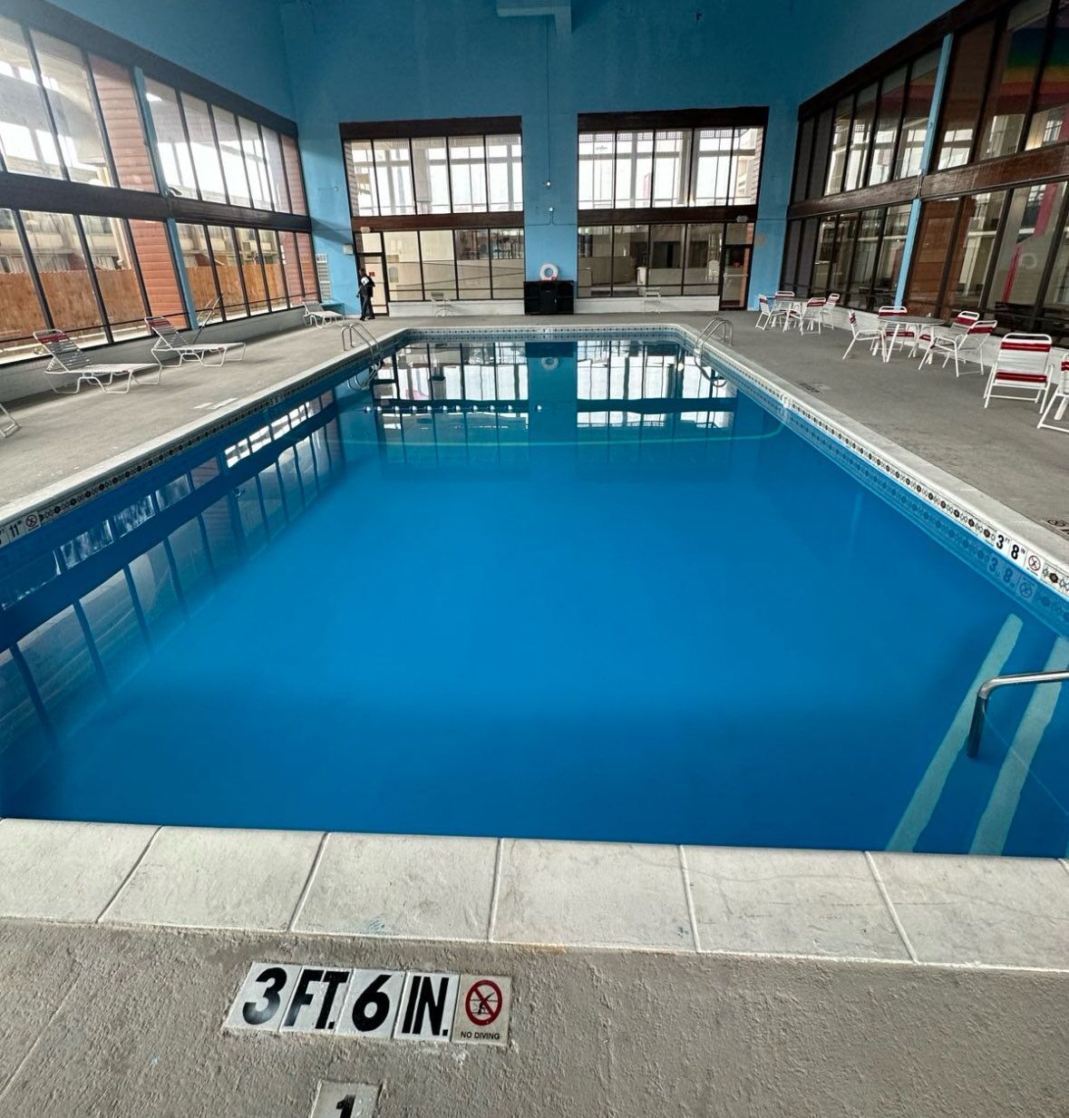 An indoor swimming pool with clear water, surrounded by windows and chairs.