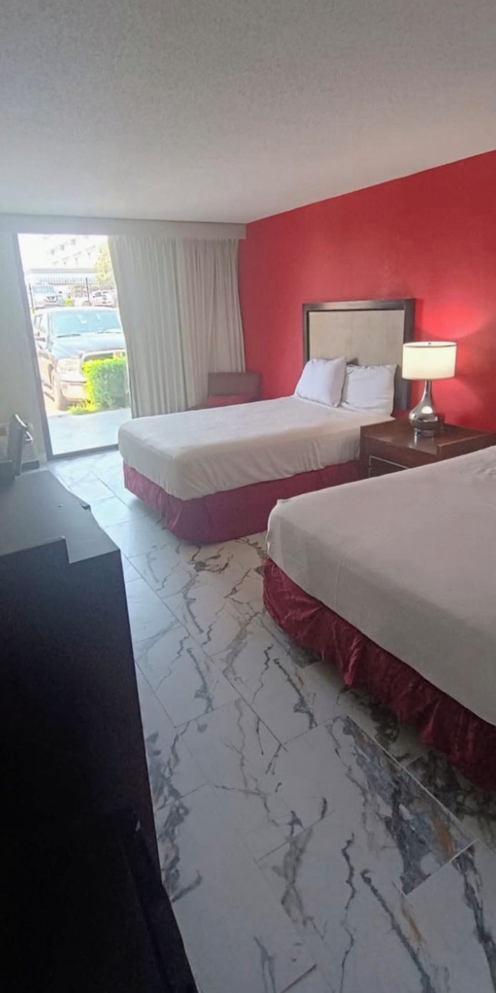 A hotel room with two beds, a desk, and a view of the outside.
