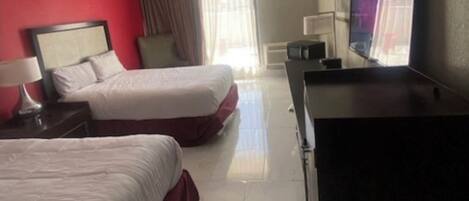 Una habitación de hotel con dos camas, un escritorio, un televisor y una ventana con cortinas.