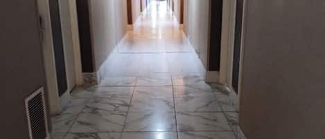 A long, narrow hallway with marble flooring and beige walls.