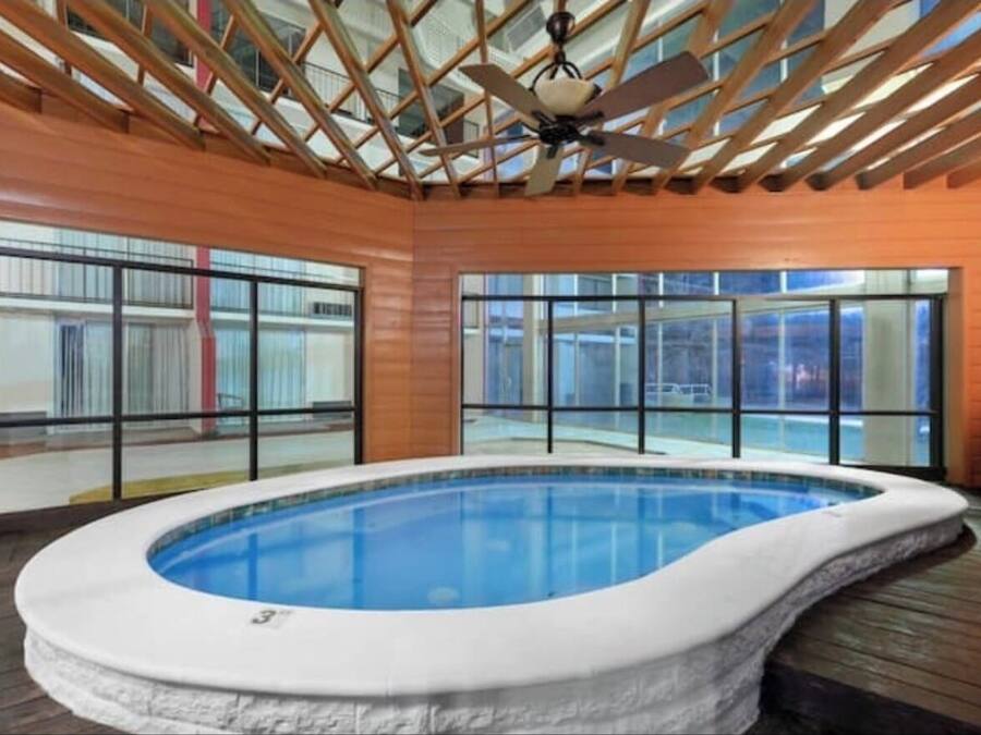 Piscina interior com teto de madeira e paredes de vidro, rodeada por um deck de madeira.