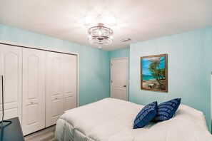 A bedroom with a bed, a painting of a beach, and a wardrobe.