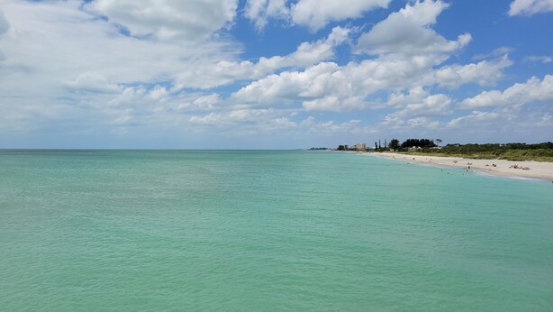 A beach with clear turquoise water, a sandy shore, and a distant building line.