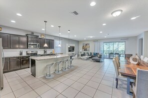 Uma cozinha moderna com armários escuros, uma ilha grande com banquetas e um espaço de jantar com mesa e cadeiras de madeira.