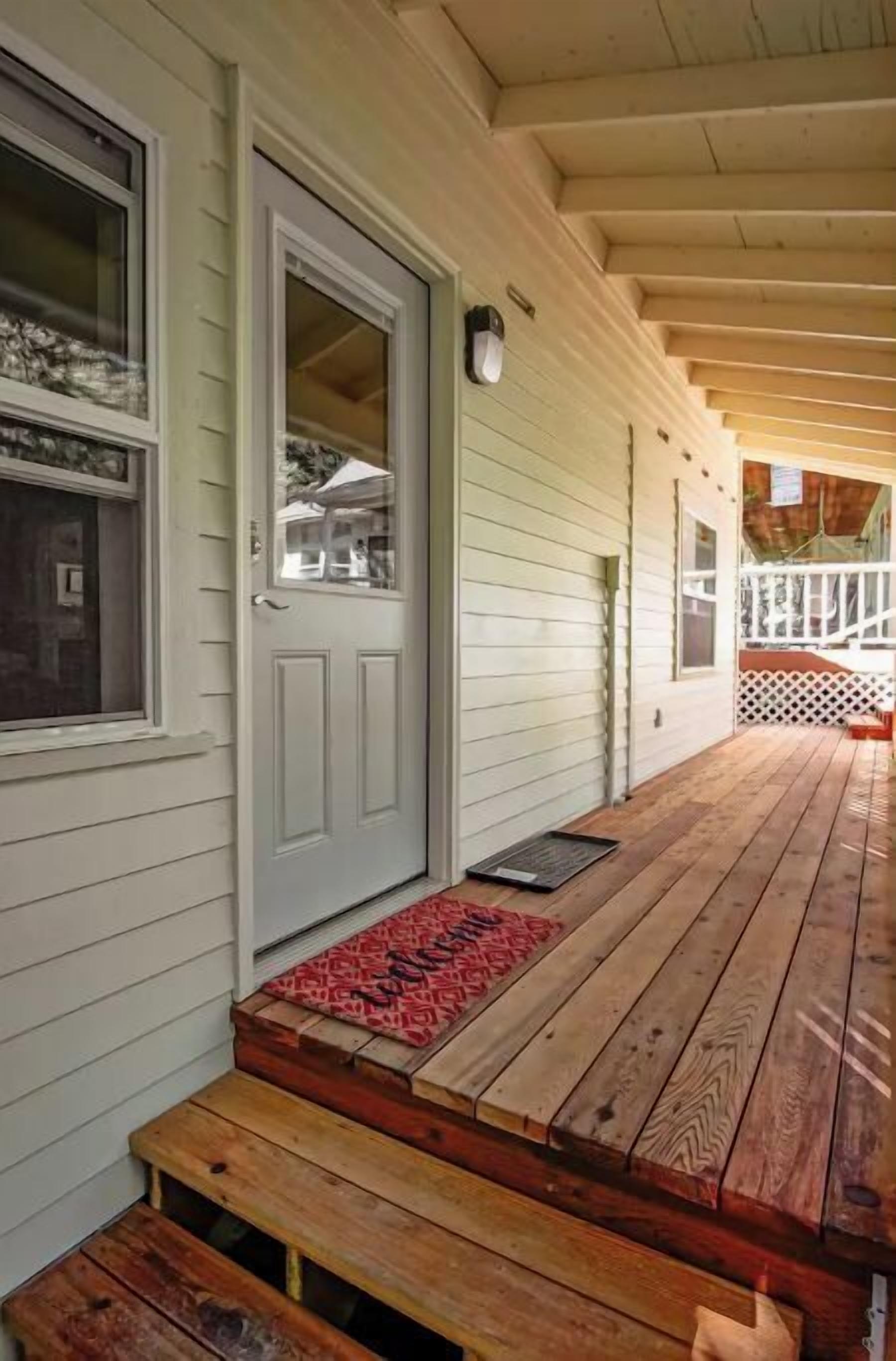 A wooden deck with a bench and a door with a red mat.