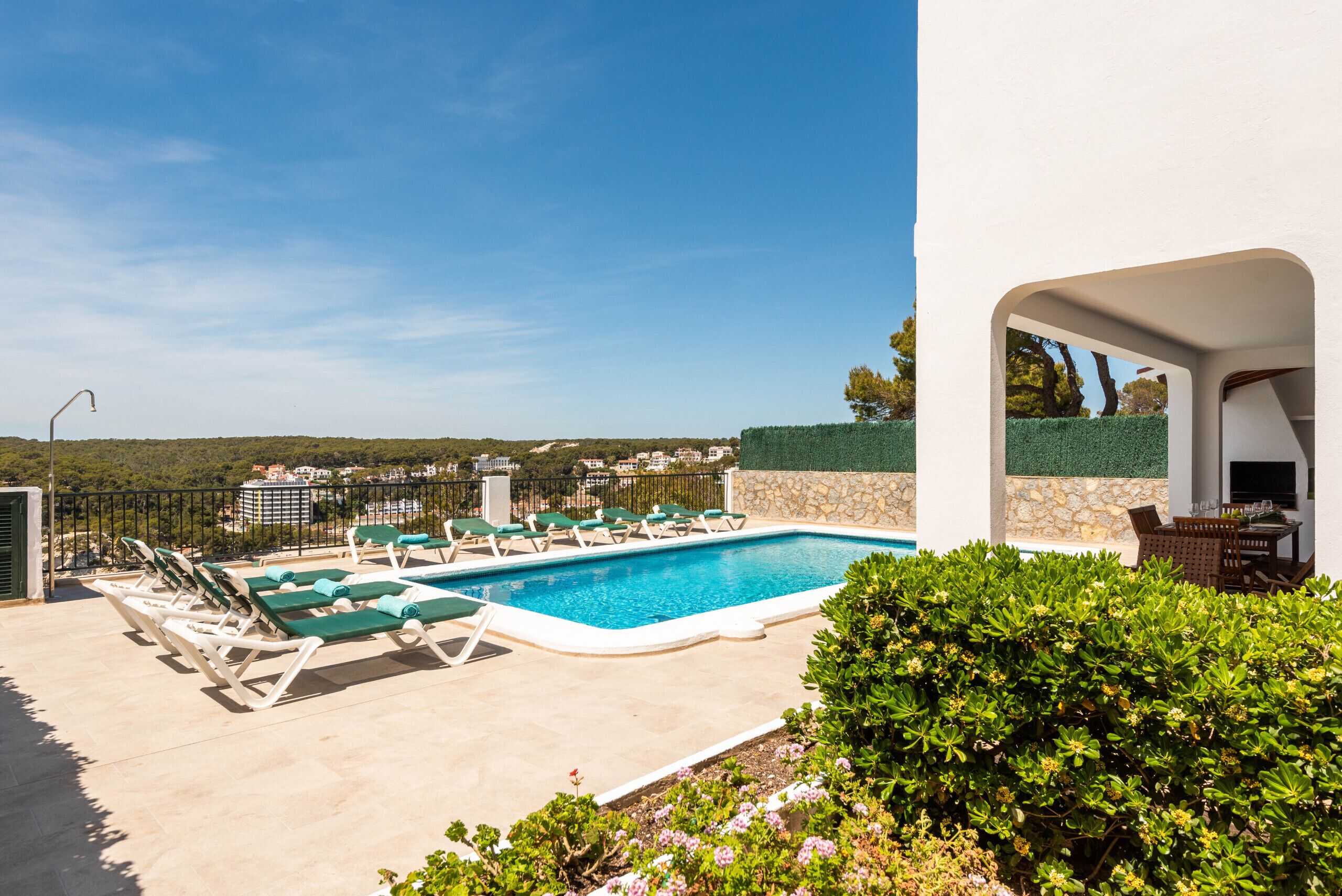 A swimming pool with lounge chairs, a stone wall, and a view of the surrounding landscape.