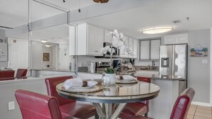 A modern kitchen with white cabinets, a round dining table with red chairs, and a visible island with a sink. - Spectacular views of the Gulf and Emerald coast - 16th floor. (Destin)