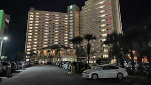 A multi-story hotel with a parking lot, palm trees, and a well-lit entrance. - Spectacular views of the Gulf and Emerald coast - 16th floor. (Destin)