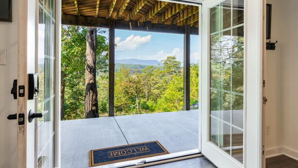 A wooden deck with a welcome mat, a glass door, and a view of a forest and mountains. - Riverfront Oasis with Mountain Views, close to town  (Middletown)