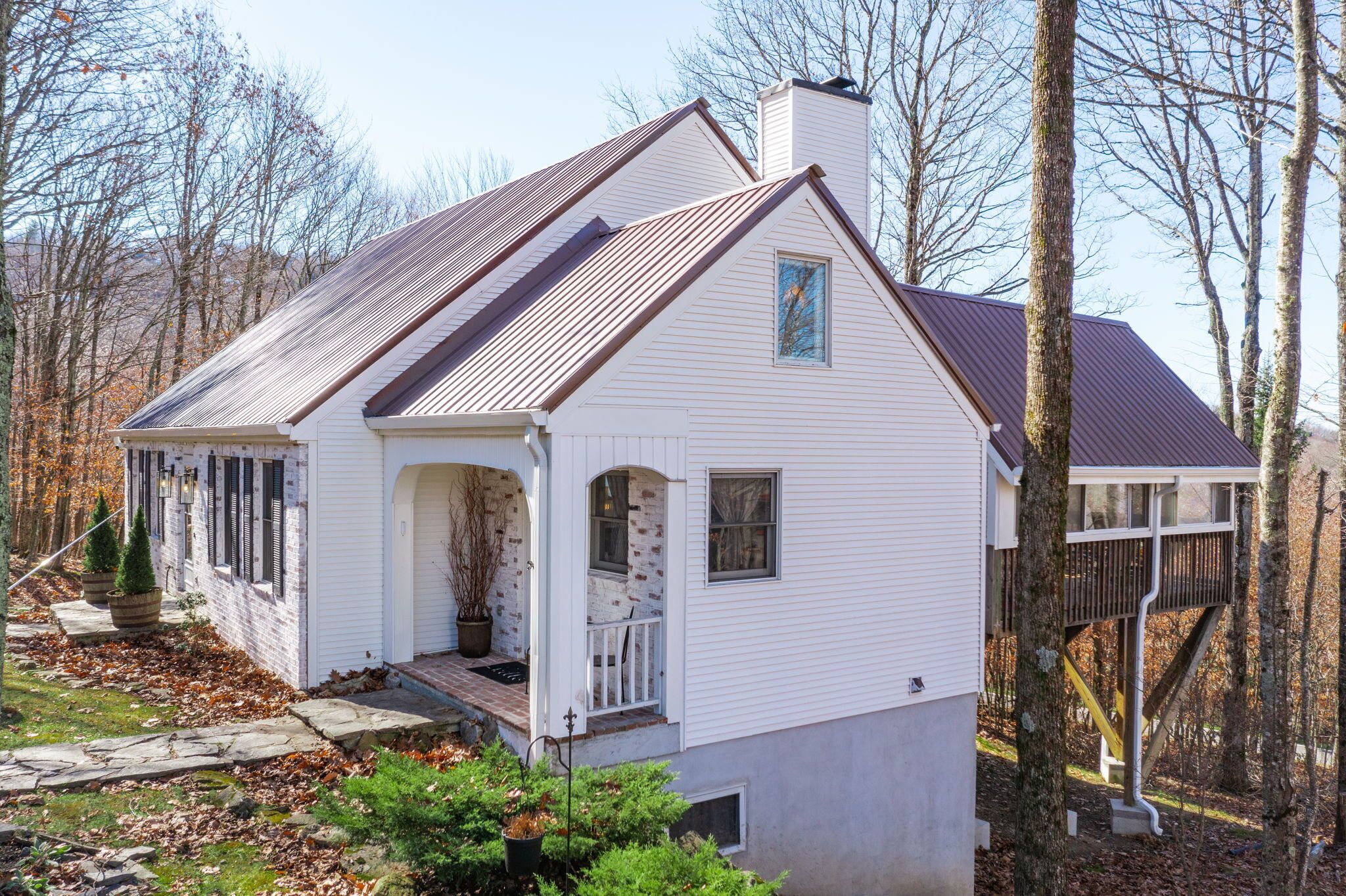 A white house with a brown roof, a front porch, and a small deck.