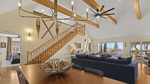 Amplia sala de estar con mesa de comedor de madera, sofá azul y escalera con barandillas de madera.