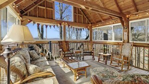 Un espacio habitable amplio y acogedor con vigas de madera, mobiliario de mimbre y grandes ventanas que ofrecen vistas al exterior.