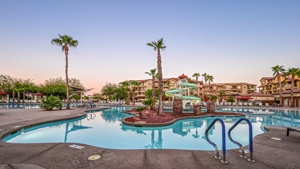 A swimming pool with a water slide, palm trees, and hotel buildings in the background.