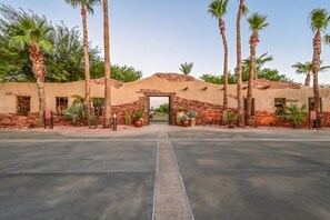 Une entrée d’immeuble avec une arche en briques, des palmiers et des plantes en pot.