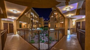 A hotel corridor with a central courtyard, featuring a gated entrance, multiple balconies, and a night-time view.