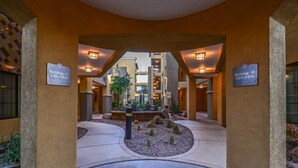 A hotel lobby with a central seating area, two building signs, and a stone fountain.