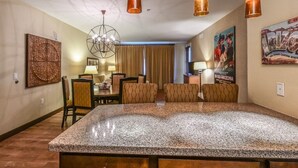 A hotel room with a large granite island, a dining area with a chandelier, and a poster on the wall.