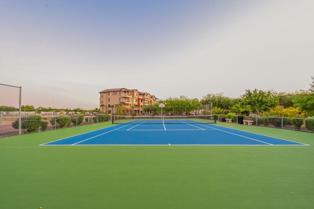 Un court de tennis en plein air, doté d’un filet, entouré de verdure et avec un bâtiment en arrière-plan.