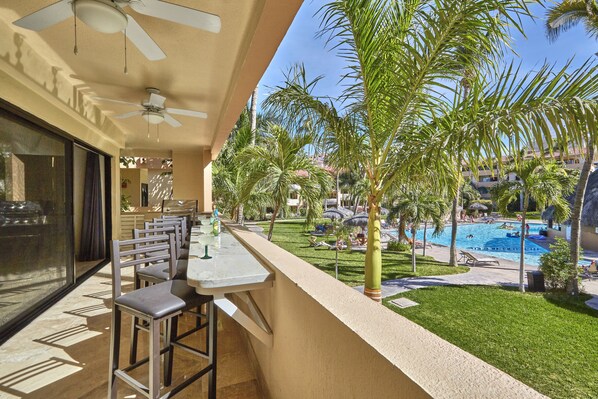 A balcony with a pool view, outdoor seating, and a ceiling fan.