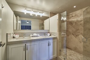 A modern bathroom with a marble vanity, a glass shower enclosure, and a large mirror above the sink. - Three Bedroom Condo Pool View, one block away from Medano Beach (Cabo San Lucas)