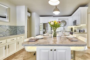 A modern kitchen with white cabinetry, a marble island, and a central vase with flowers.