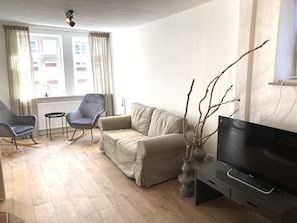 A living room with a beige sofa, two rocking chairs, a small table, a TV, and a vase with branches.