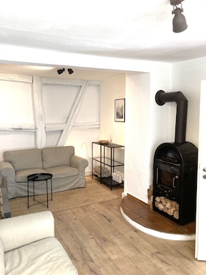 A cozy living room with a sofa, a small table, a black wood-burning stove, and a framed picture on the wall.