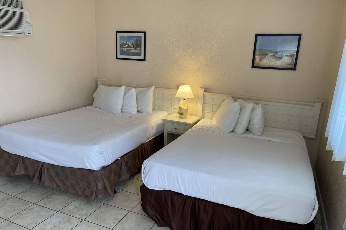 A hotel room with two beds, a nightstand with a lamp, and two framed pictures on the wall.
