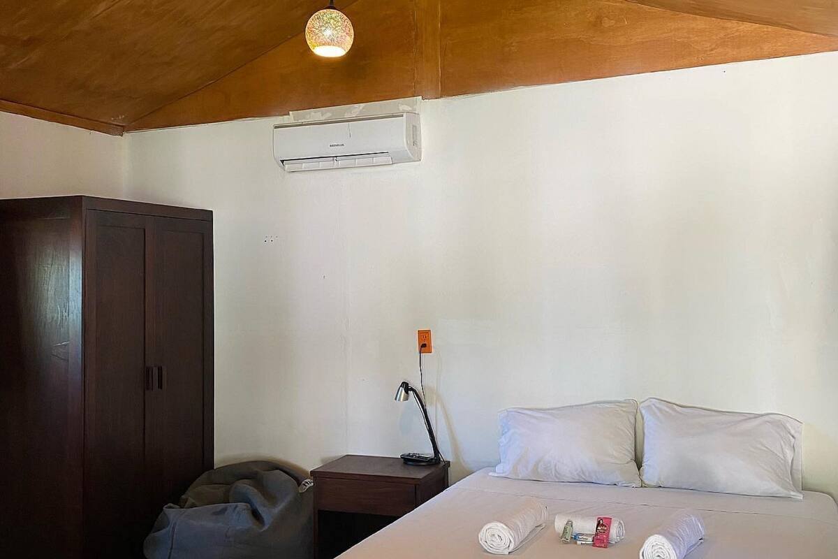 Une chambre avec un plafond en bois, un lit avec du linge de lit blanc, un bureau avec une lampe et une armoire.