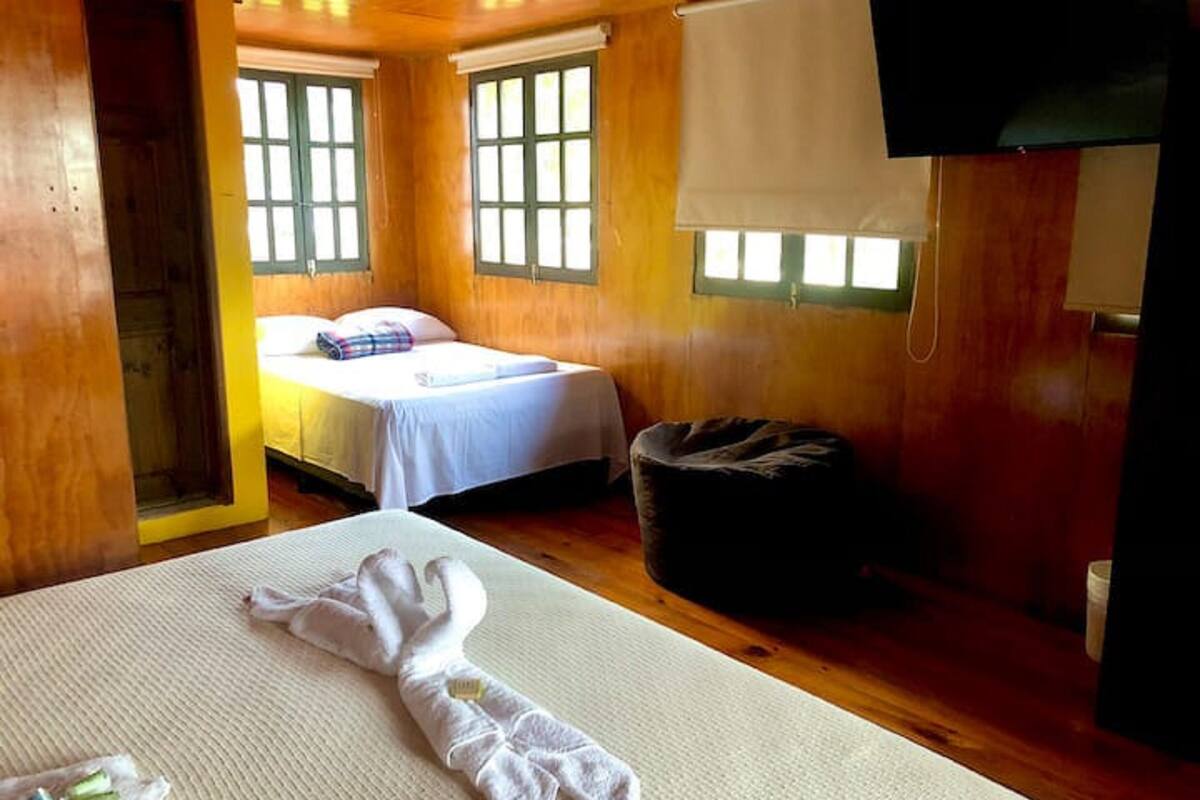 Une pièce aux murs en bois, un lit avec une literie blanche, un petit canapé et un téléviseur fixé au mur.