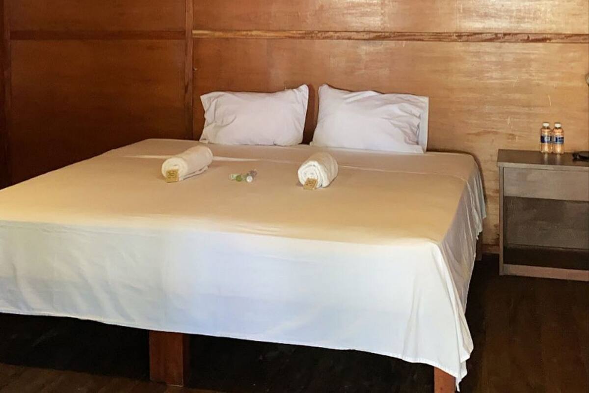 Une pièce en bois avec un lit, des oreillers, une table de chevet et un luminaire suspendu.