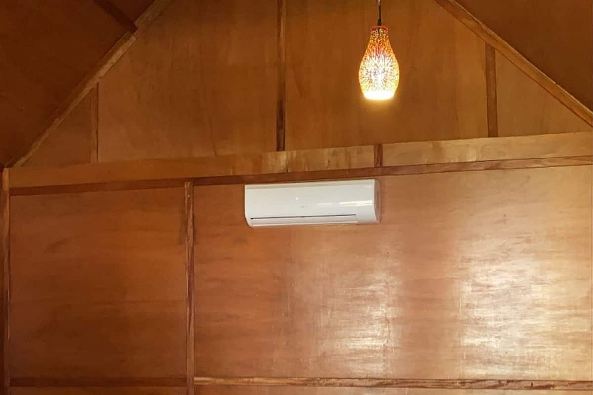 Une pièce aux murs lambrissés, comprenant un lit, des oreillers, une table de chevet et un luminaire suspendu.