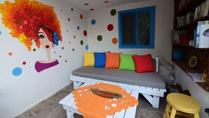 Una habitació amb un mural colorit, un sofà amb coixins multicolors, una taula petita amb una decoració de peix i una biblioteca plena de llibres.