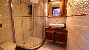 Un bany modern amb plat de dutxa envoltat de vidre, un lavabo blanc, mobles de fusta i un mirall gran.