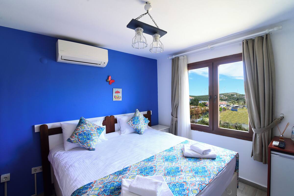 A bedroom with a large bed, a window with a view, and a ceiling fan.