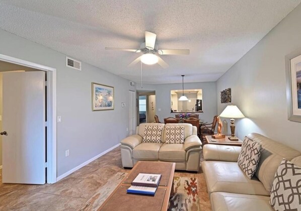 A living room with a ceiling fan, a dining area with a table and chairs, and a sofa with patterned cushions. - Shorewalk "A Little Piece of Paradise" close to beaches, golf, restaurants, IMG (Bradenton)