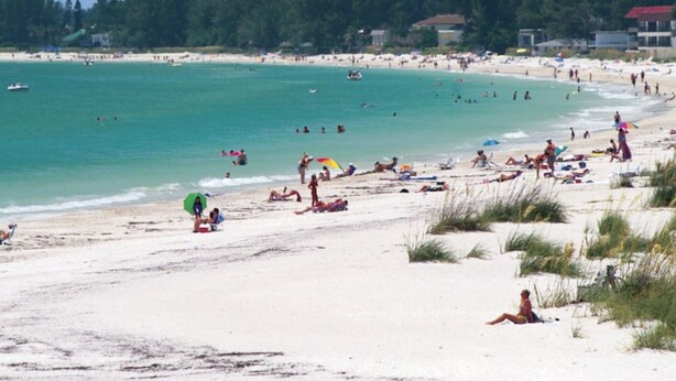 A beach with people sunbathing and swimming, surrounded by greenery and buildings. - Shorewalk "A Little Piece of Paradise" close to beaches, golf, restaurants, IMG (Bradenton)