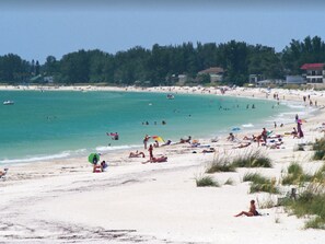 A beach with people sunbathing and swimming, surrounded by greenery and buildings. - Shorewalk "A Little Piece of Paradise" close to beaches, golf, restaurants, IMG (Bradenton)