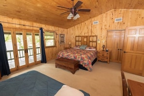 A wooden cabin bedroom with a bed, a bench, a nightstand, and a ceiling fan.