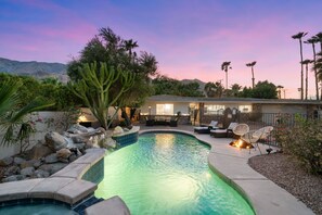 Une piscine bordée de pierres, entourée d’une terrasse aménagée avec du mobilier d’extérieur et agrémentée d’une petite cascade.