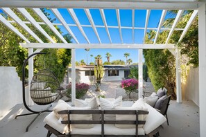 Un espace extérieur aménagé, abrité et doté d’une pergola, d’un fauteuil suspendu et d’une vue sur une maison avec un jardin.