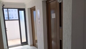 Un pasillo con suelo de baldosas, un ventilador de techo y dos puertas con un cartel en la pared.