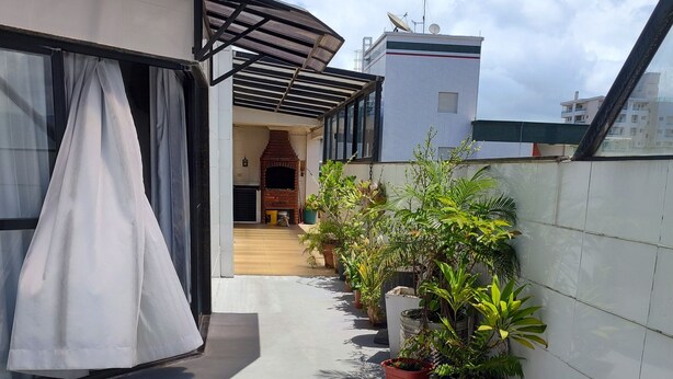 Terraza en la azotea con chimenea de ladrillo, plantas en macetas y una zona cubierta con cortina blanca.