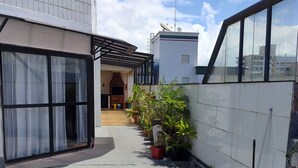 Un sendero de hormigón estrecho bordeado por edificios, con plantas en macetas y una escoba apoyada en una pared.