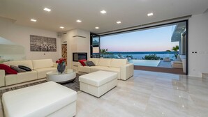 A modern living room with a large glass door leading to a balcony with a view of the sea.