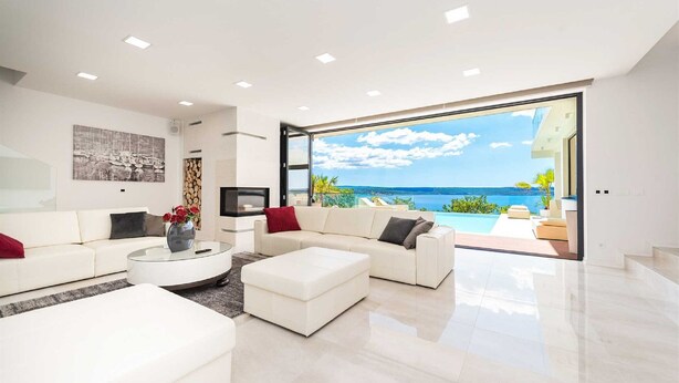 A modern living room with a large glass door leading to a balcony with a view of the sea.