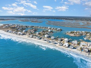 An aerial view of a coastal residential area with houses, a beach, and a marina.