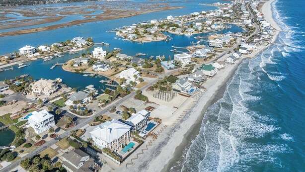 Vue aérienne d’une zone de villégiature côtière comprenant plusieurs bâtiments, une plage et un port de plaisance.