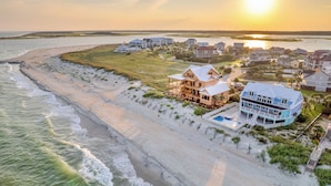 Un quartier résidentiel situé sur la côte, avec des propriétés donnant sur la plage, notamment une maison avec piscine et une autre dotée d’une grande véranda.
