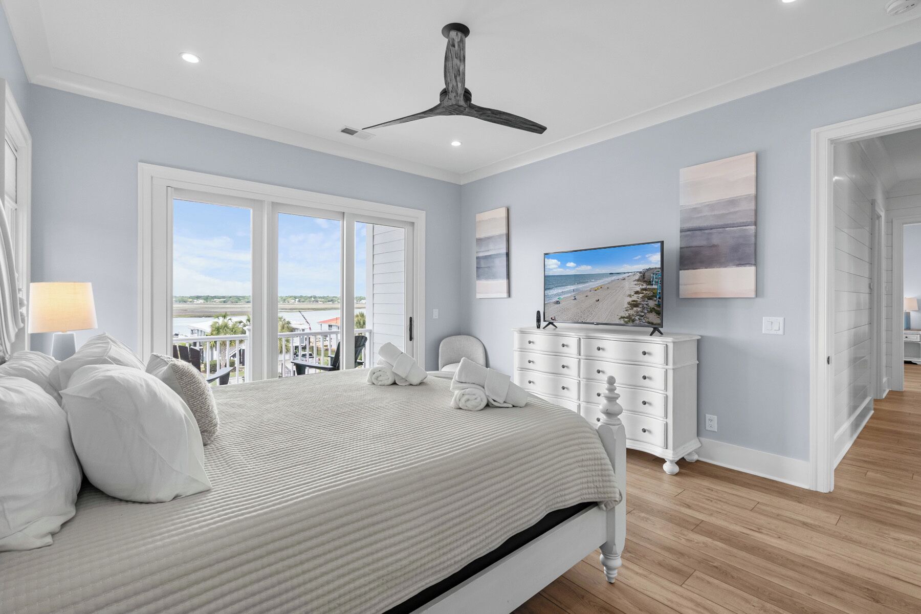 A bedroom with a large bed, a ceiling fan, a dresser, and a TV.